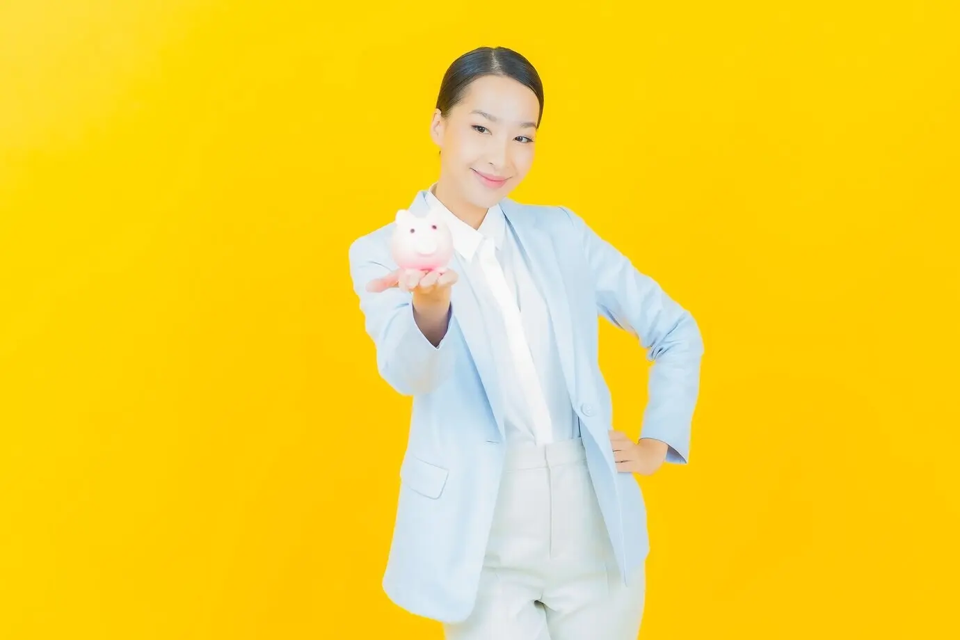 Porträt einer schönen jungen asiatischen Frau mit einem Sparschwein vor gelbem Hintergrund.