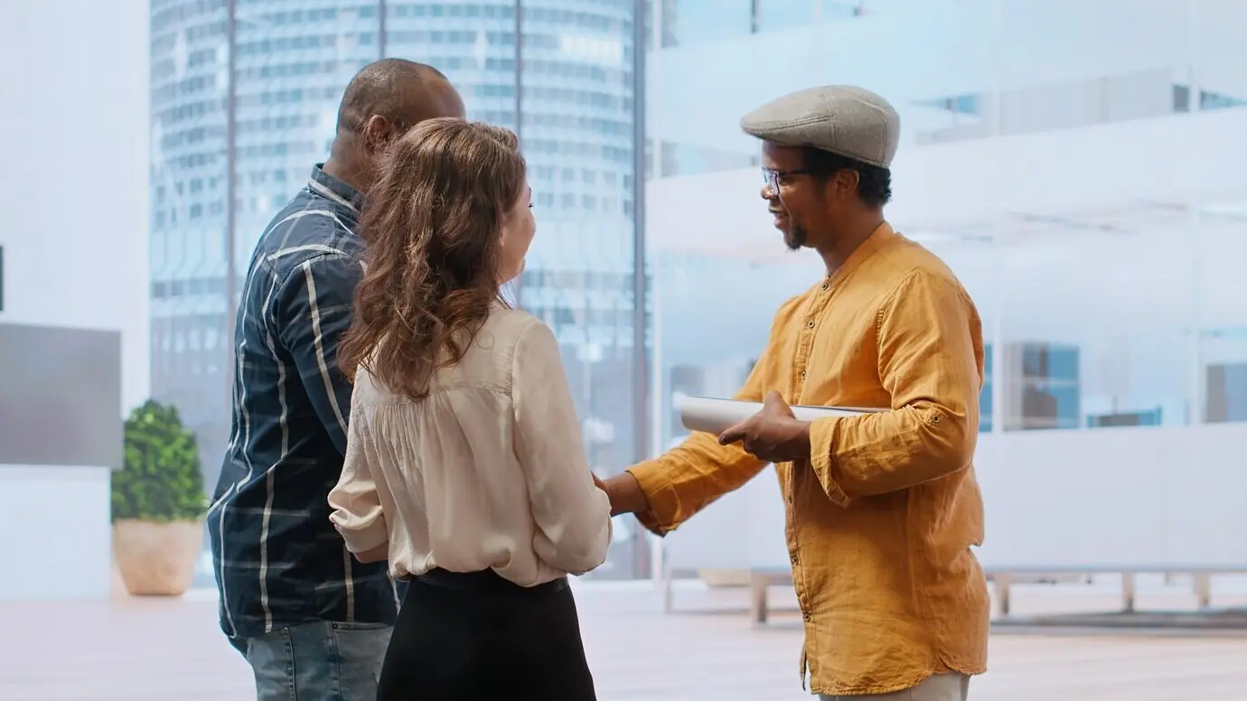 Kunden und ein Immobilienmakler auf einem Bürorundgang, bei dem sie die moderne Arbeitsplatzgestaltung beurteilen.